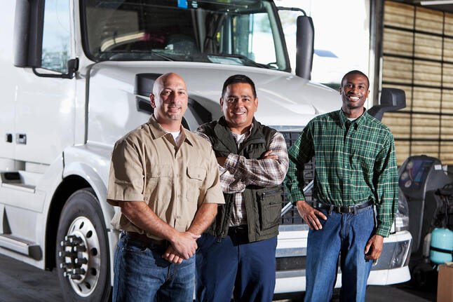 3 motor carrier professionals standing in front a semi smiling  